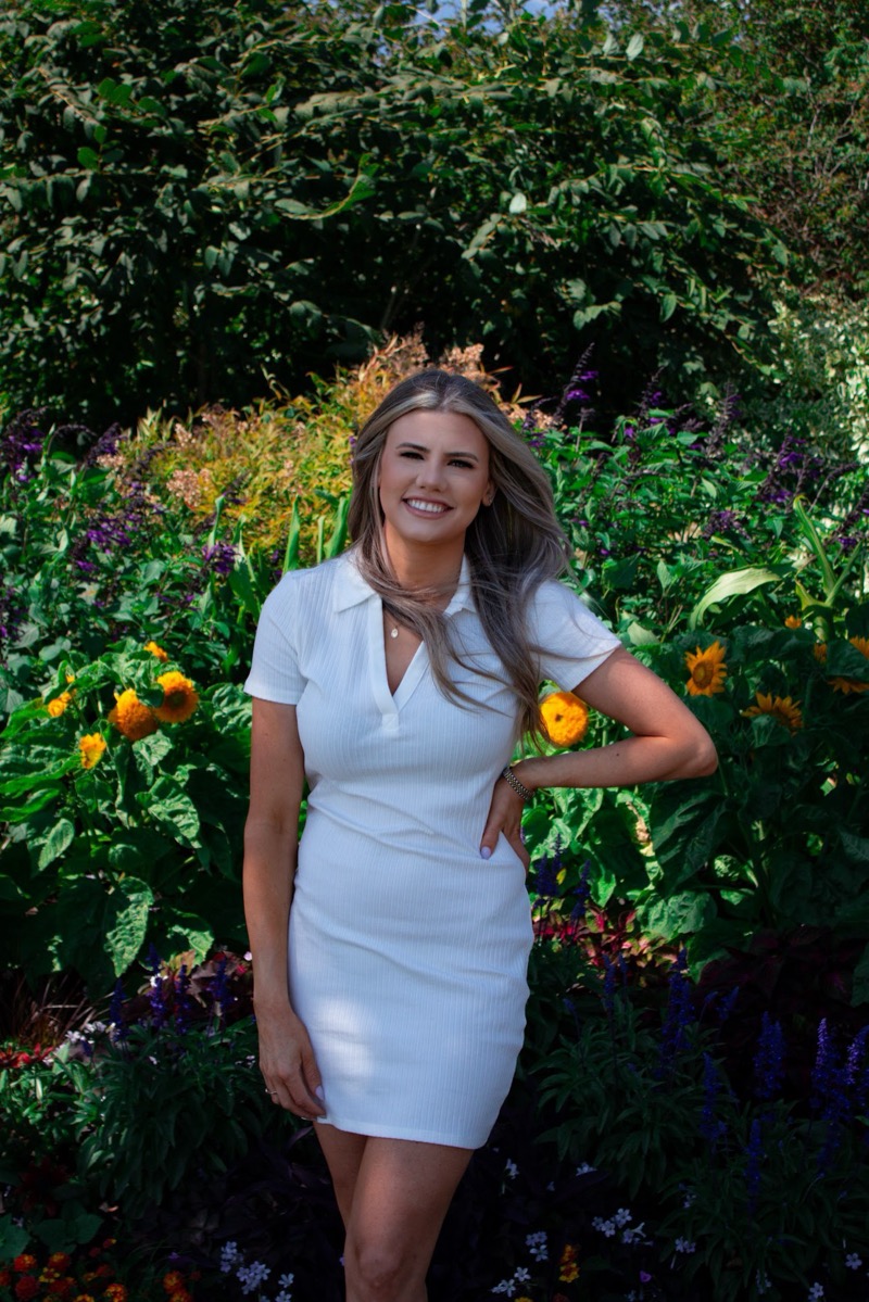 Founder of Scope Social, Vraya Forrest standing in front of a bed of bright flowers.